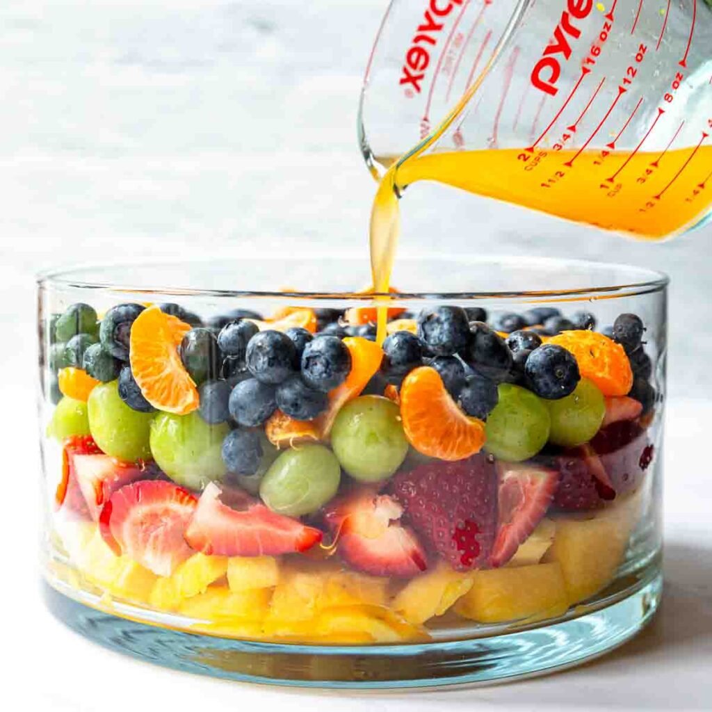pouring a citrus glaze over a bowl of fresh fruit