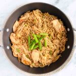 Green onion slices topping chicken lo mein in a wok.