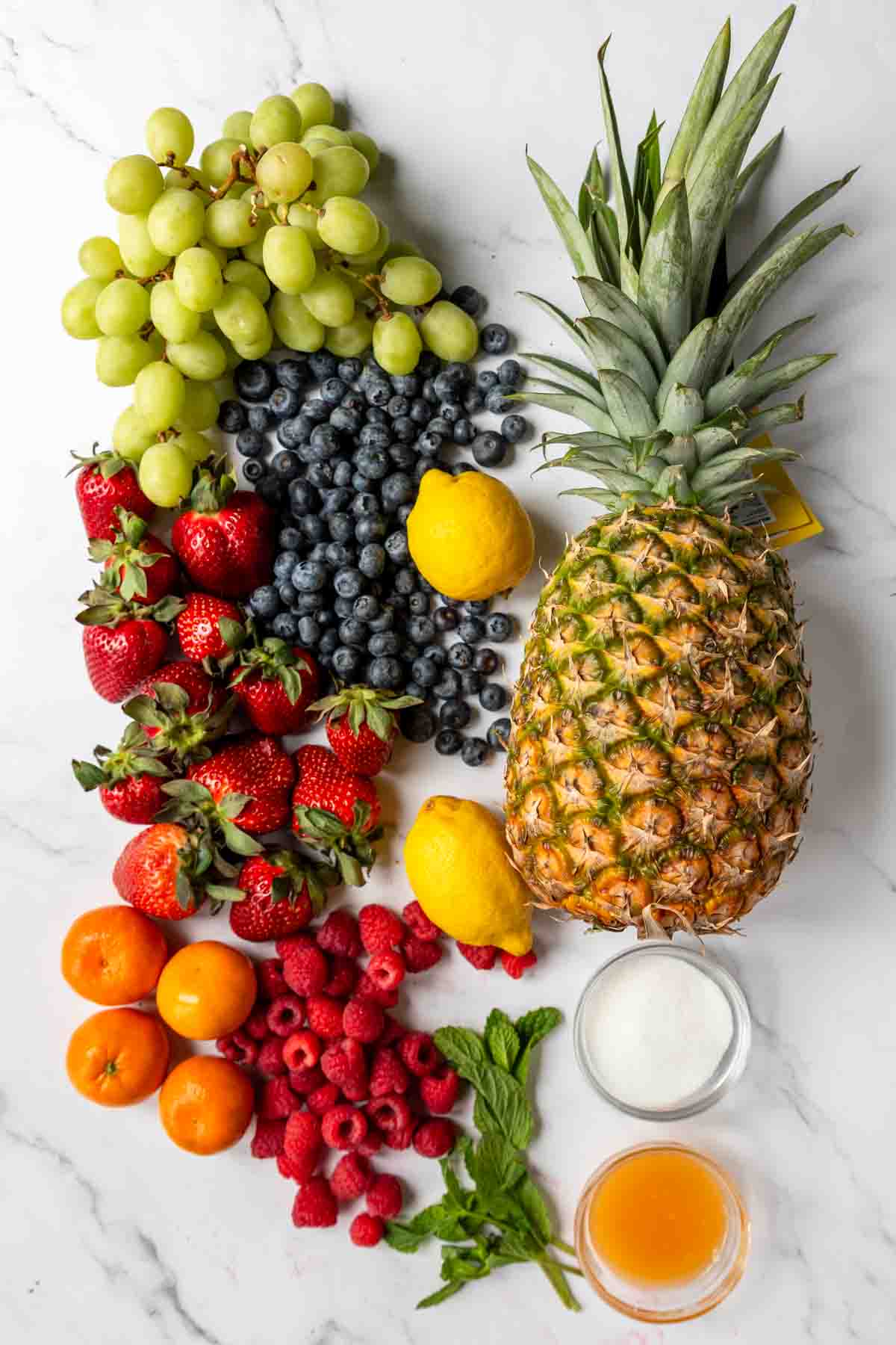 fresh fruit to make fruit salad on a table ; pineapple, strawberries, blueberries, grapes, clementines, etc...
