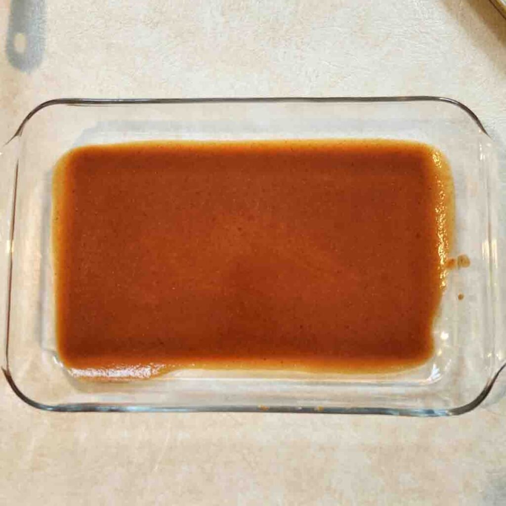 Red enchilada sauce coating the bottom of a glass baking dish.