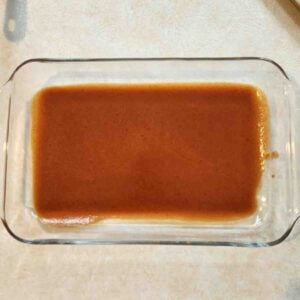 Red enchilada sauce coating the bottom of a glass baking dish.