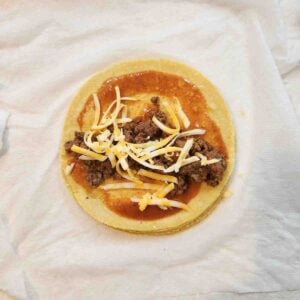 Red sauce, ground beef and shredded cheese topping a yellow corn tortilla.