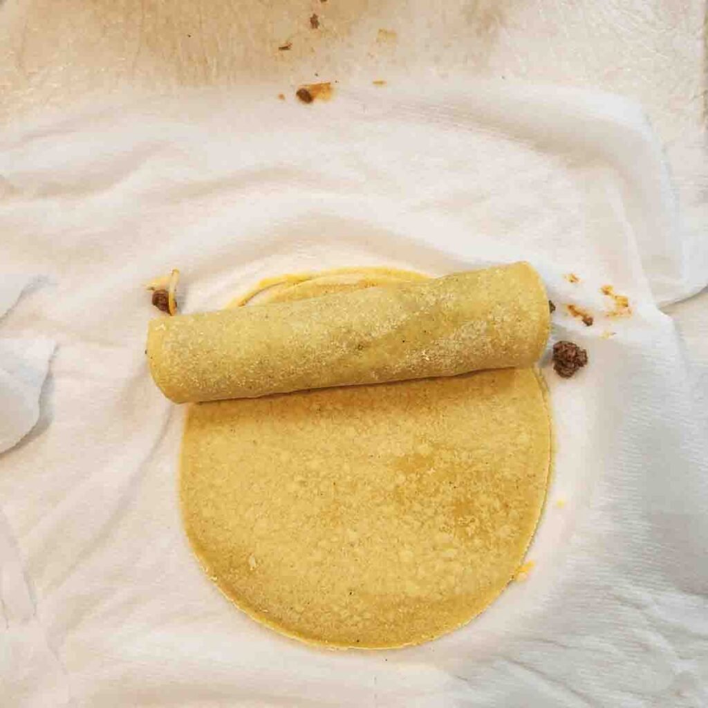 Corn tortillas being wrapped up with ground beef mixture.