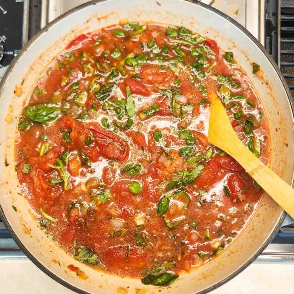 Wooden spoon resting in basil and tomato mixture.