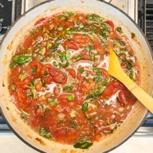 Wooden spoon resting in basil and tomato mixture.
