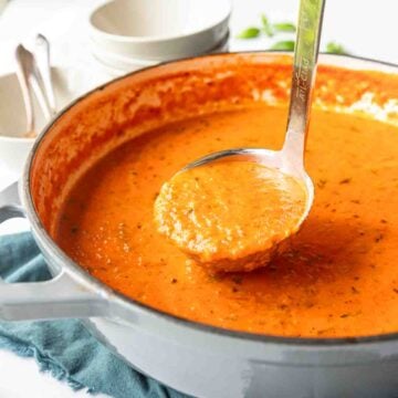 Ladle pulling up out of a Dutch oven with creamy roasted tomato basil soup.