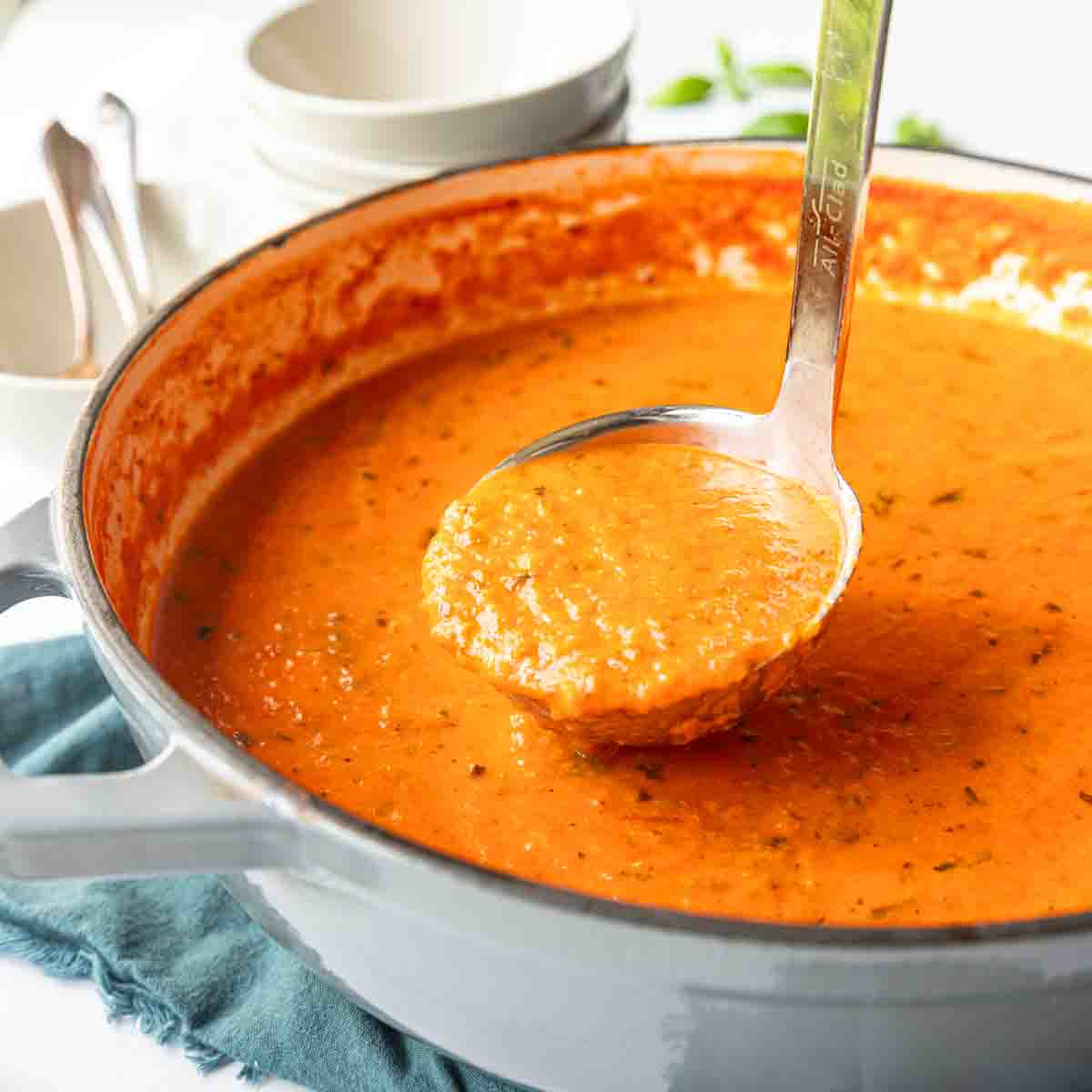 Ladle pulling up out of a Dutch oven with creamy roasted tomato basil soup.