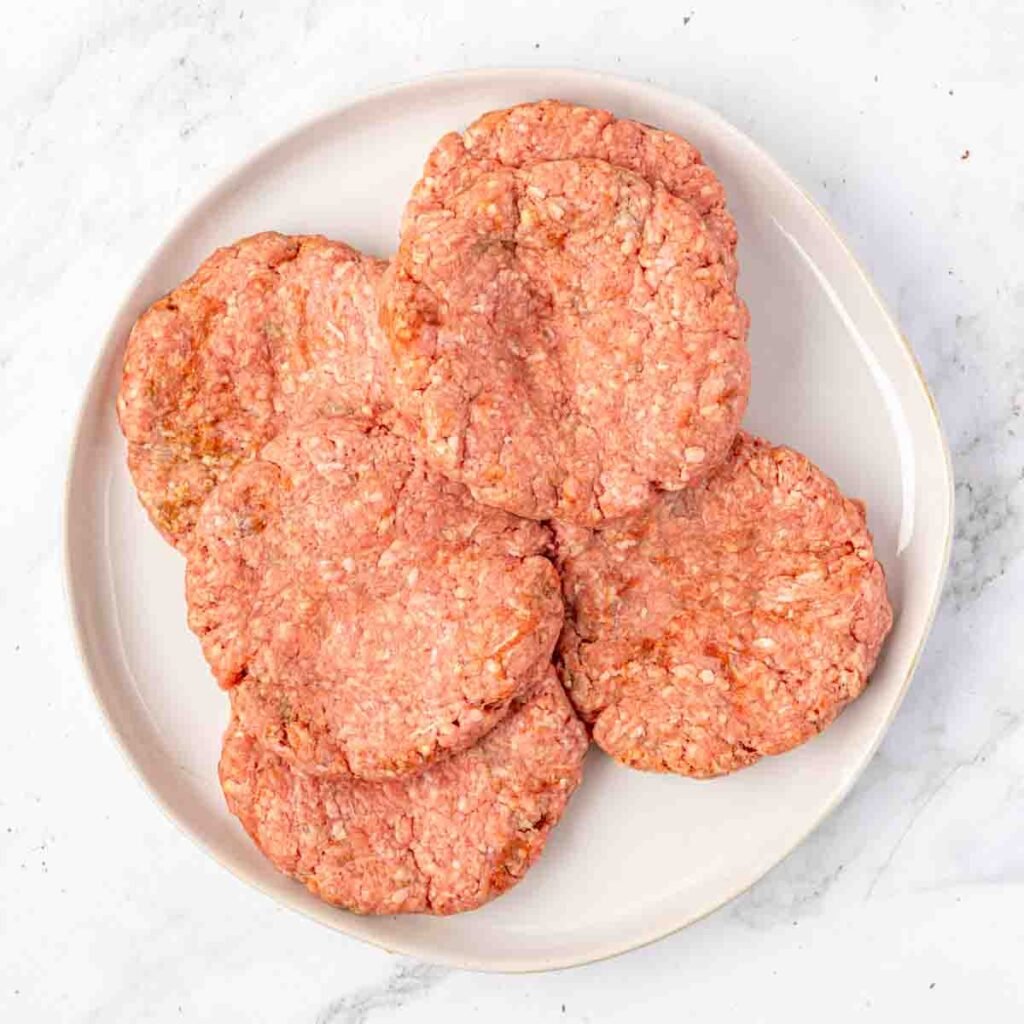 Raw ground beef patties on a plate ready to cook.