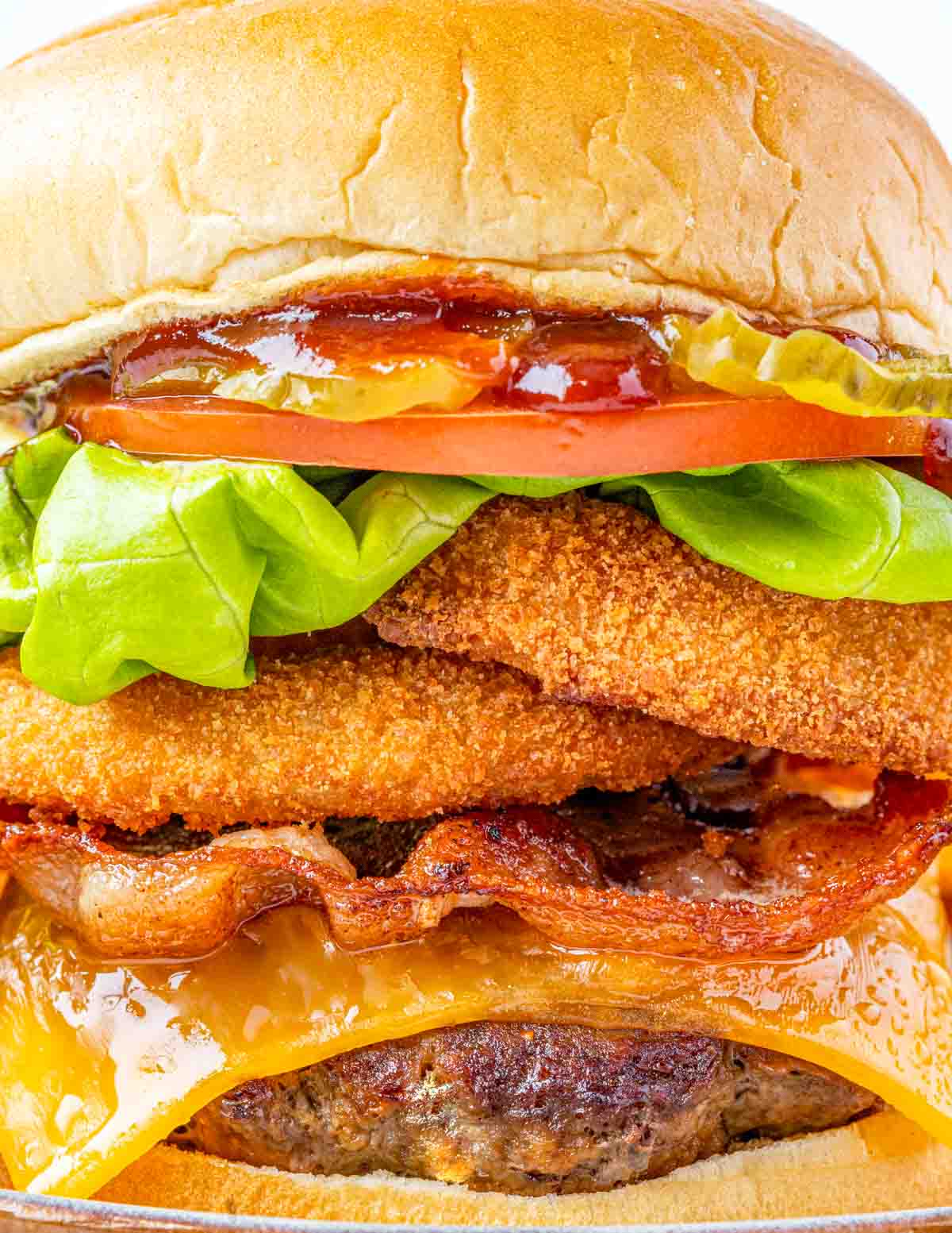 Close up of a barbecue bacon cheeseburger with onion rings, tomato, lettuce and pickles.