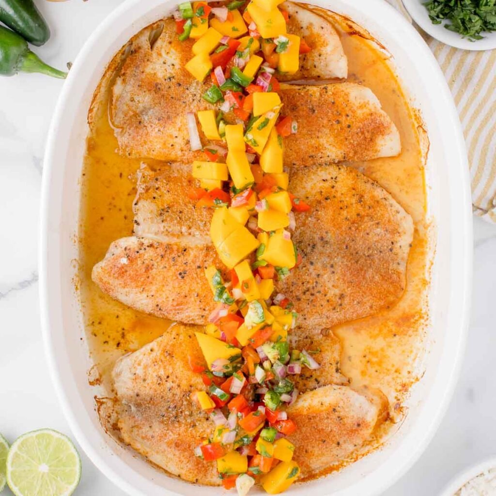 Tilapia baked in a white dish with fresh mango salsa over top