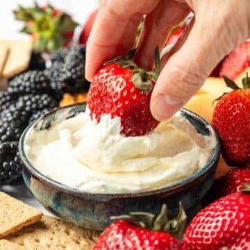 A hand dipping a strawberry into marshmallow fruit dip