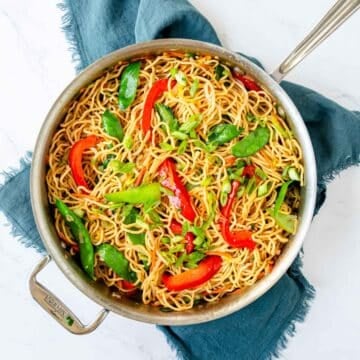Top view of a prepared Veggie Lo Mein in a skillet with snow peas and bell peppers.