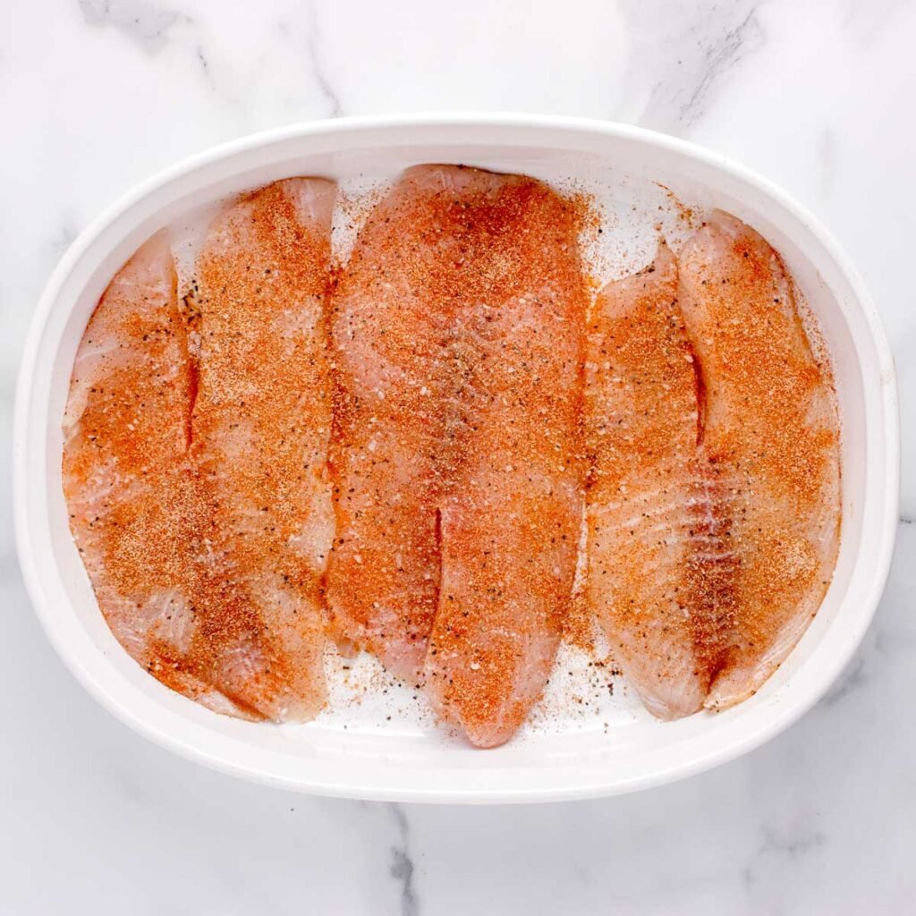 raw tilapia in a baking dish with seasoning