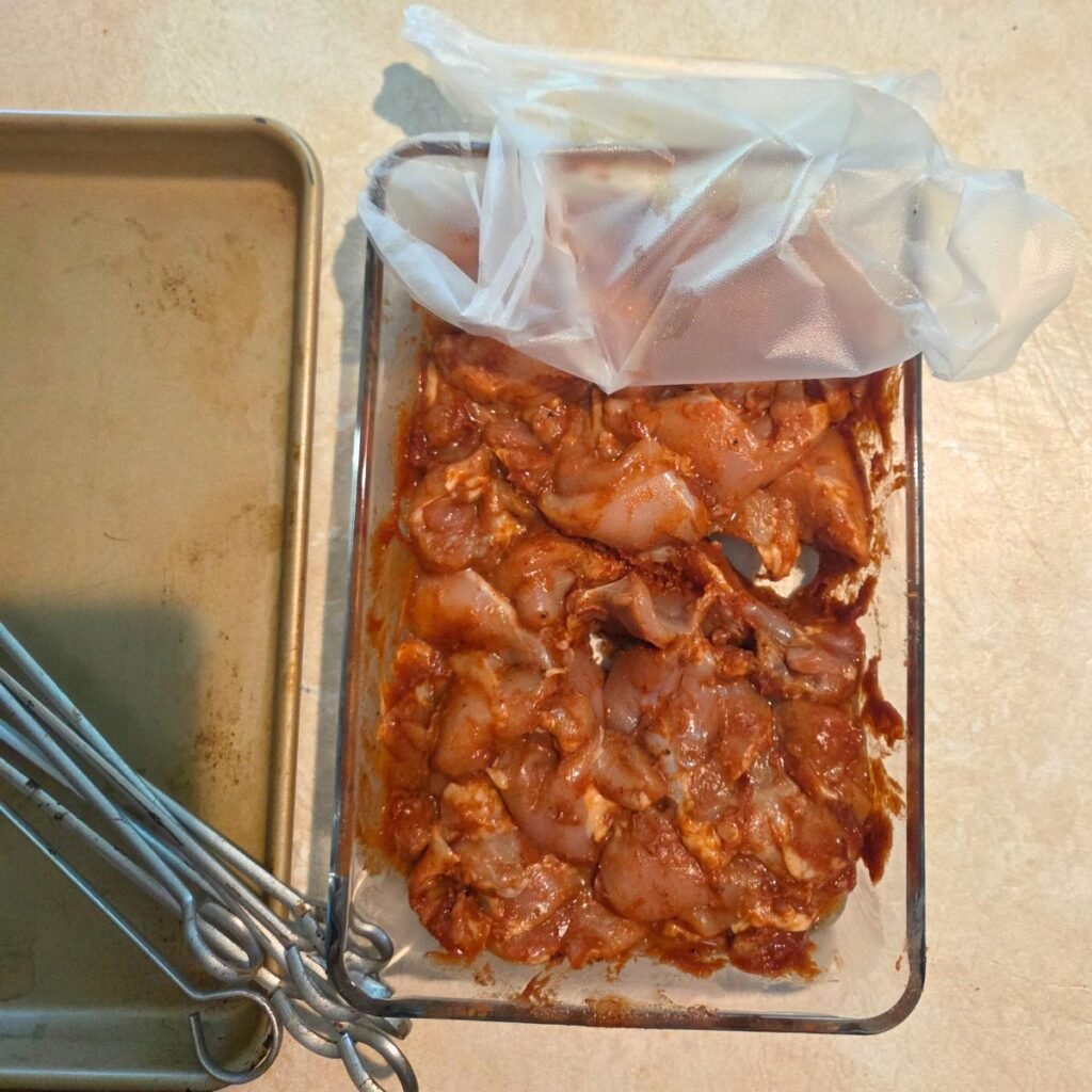 Chicken marinade coating the chicken thigh chunks in a glass container.
