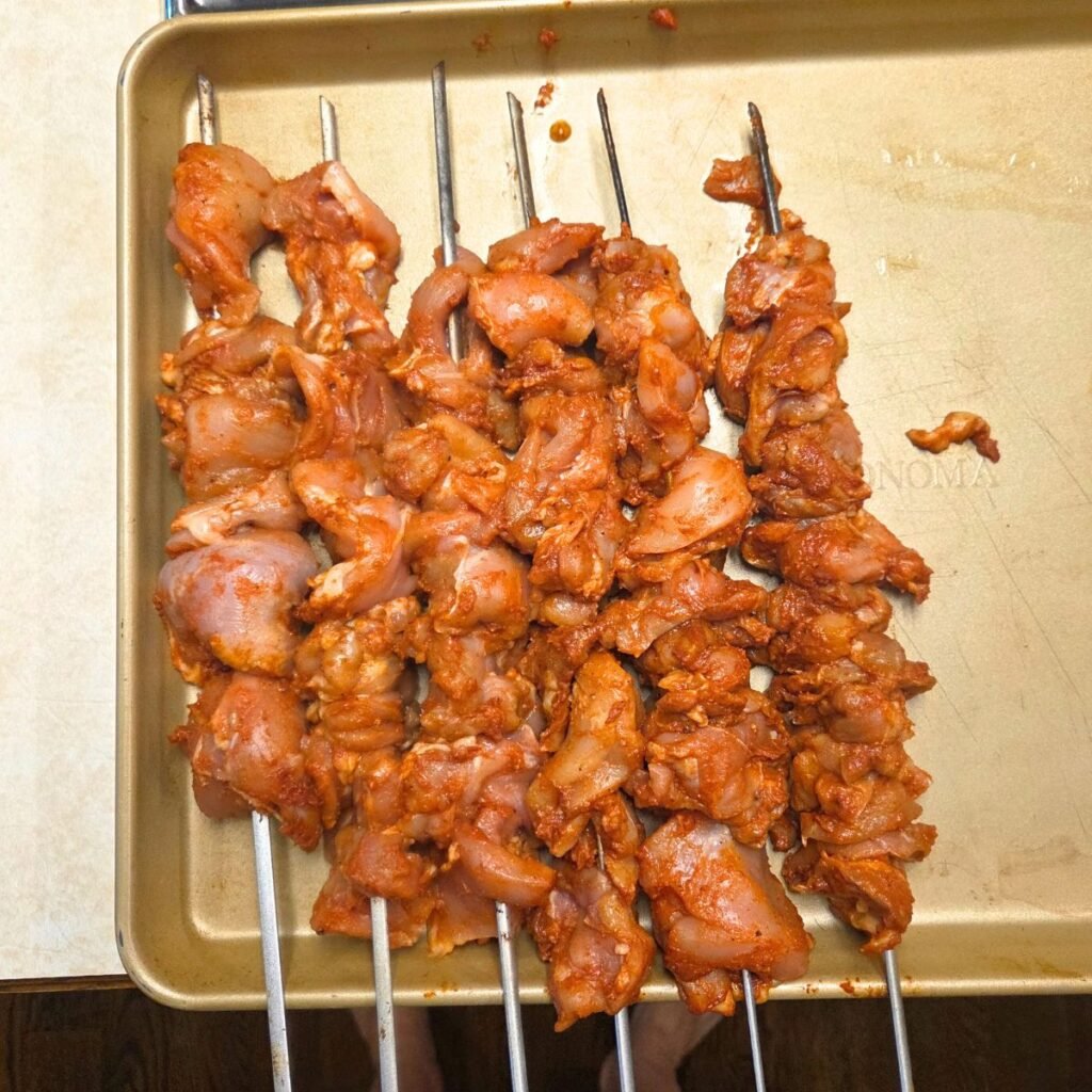 Marinated chicken thighs added to metal skewers.