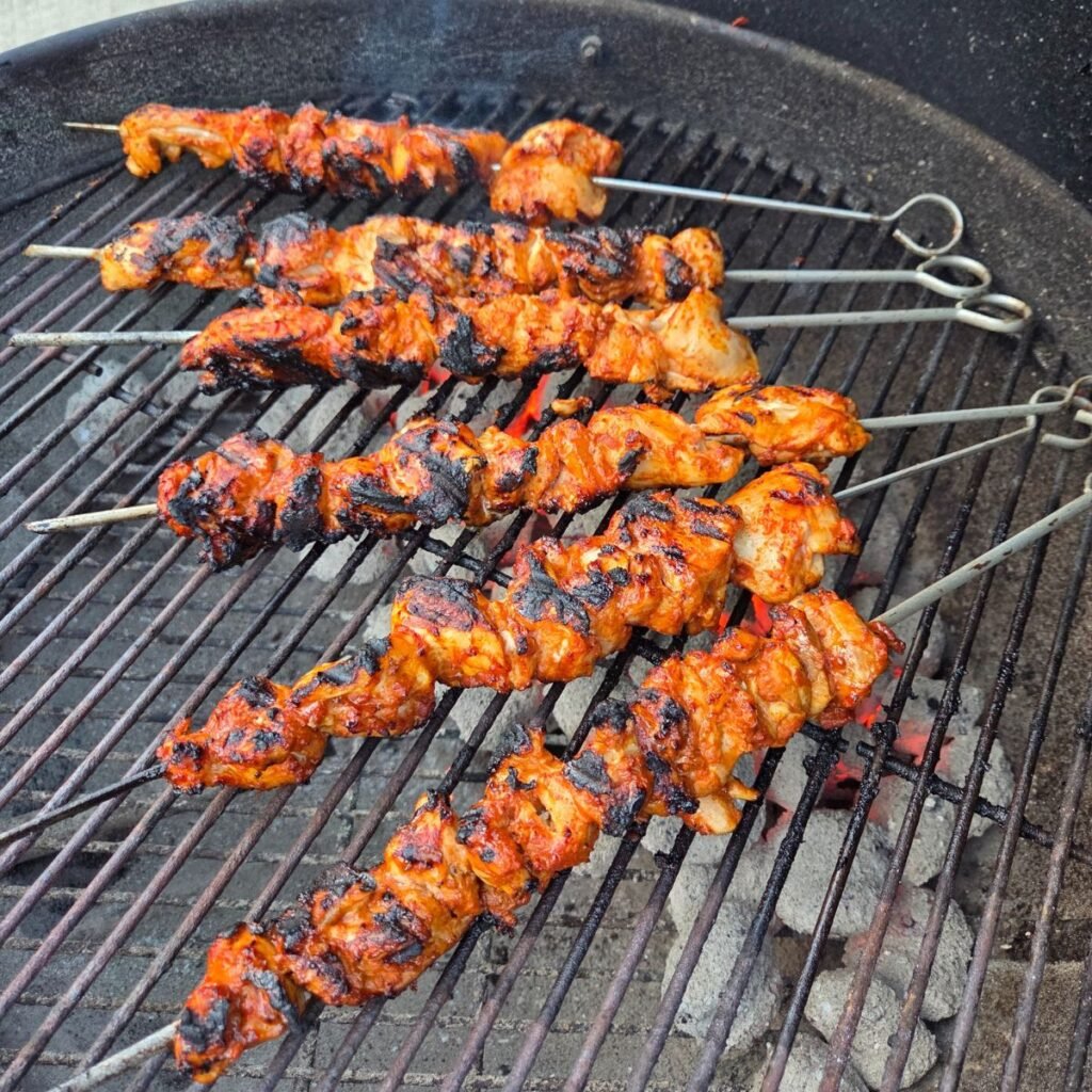 Grilled chicken thigh skewers on a hot charcoal grill.