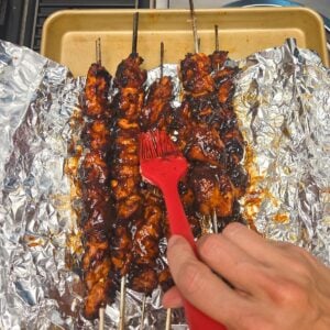 Baster adding bbq sauce to the chicken grilled chicken skewers.