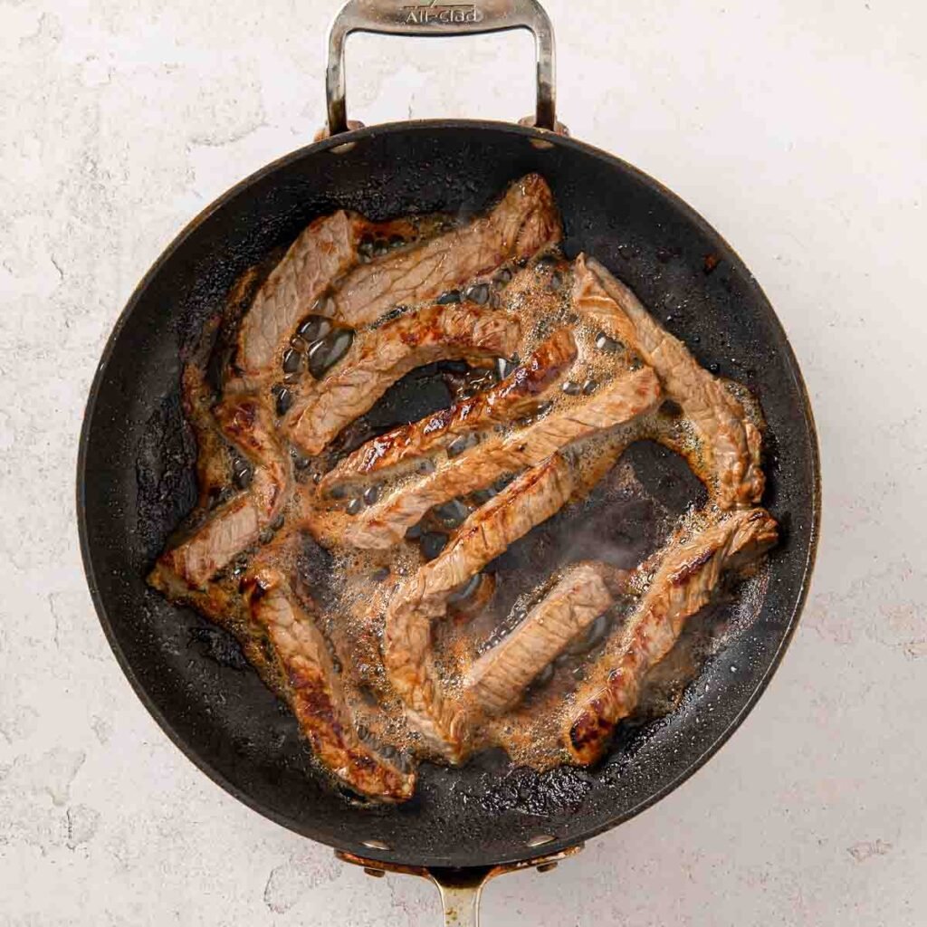 Strips of steak frying in a skillet.