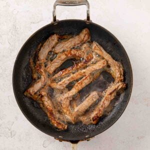 Strips of steak frying in a skillet.