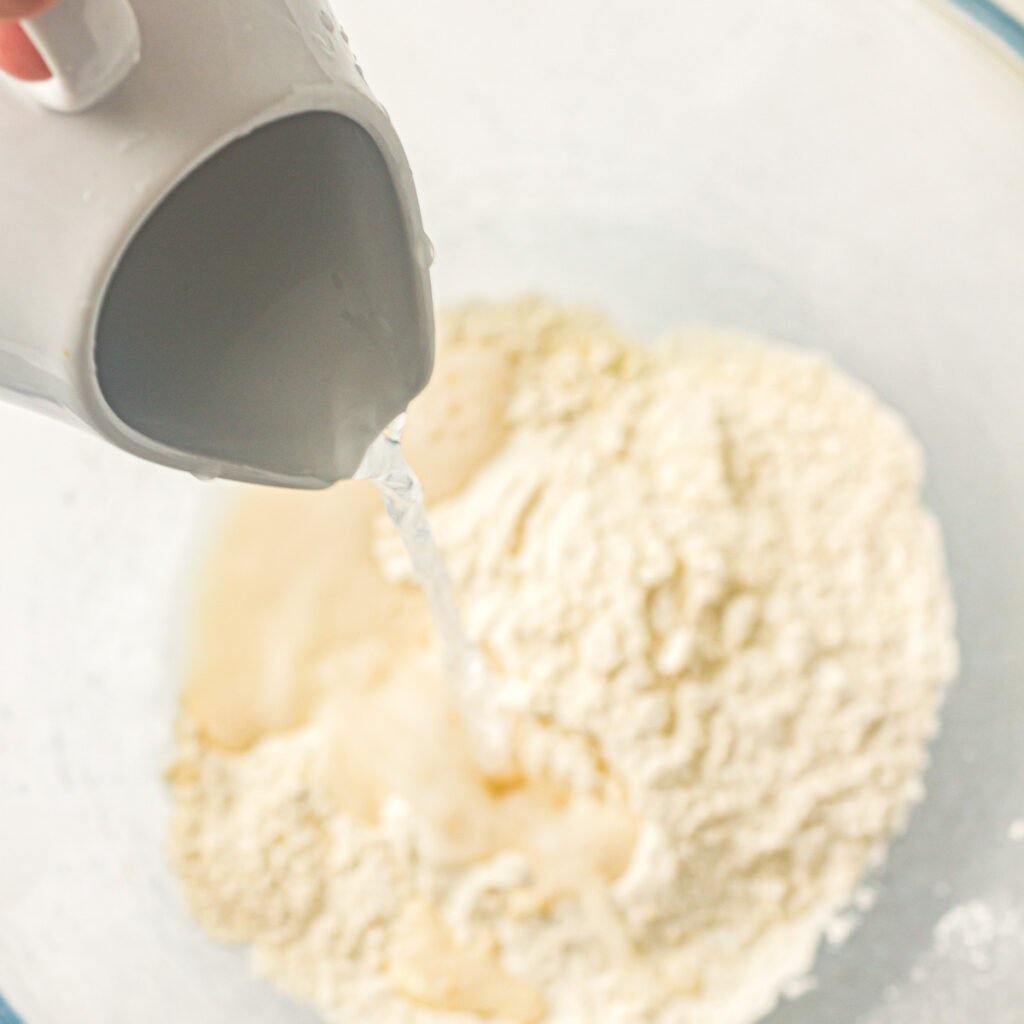 Water being poured into a glass mixing bowl of dry ingredients to make homemade pancakes.