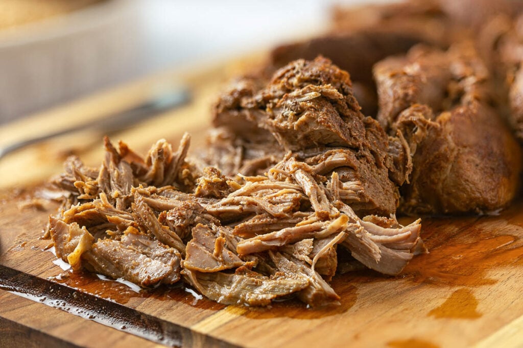 Juicy, tender pieces of pulled pork shredded to small pieces resting in its juices on a cutting board, before serving.