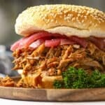 Pulled pork sandwich coated in barbecue sauce served on a sesame bun topped with pickled onions.