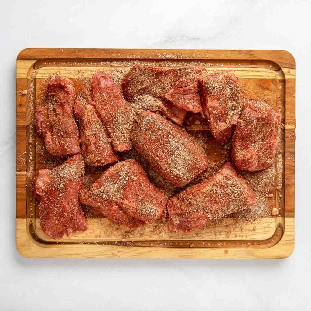 Pork butt seasoned with a dry rub on all sides, resting on the cutting board.