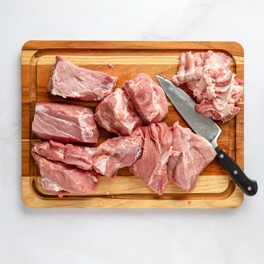 Pork butt cut into large chunks with the fat removed on a wooden cutting board.