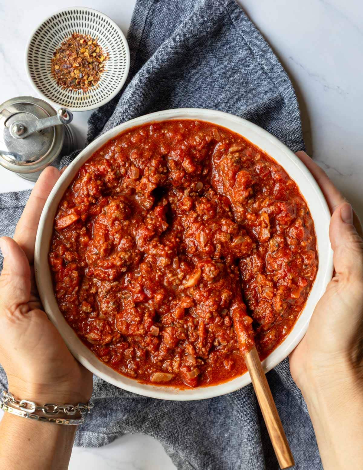 two hands holding a bowl of beef bolognese