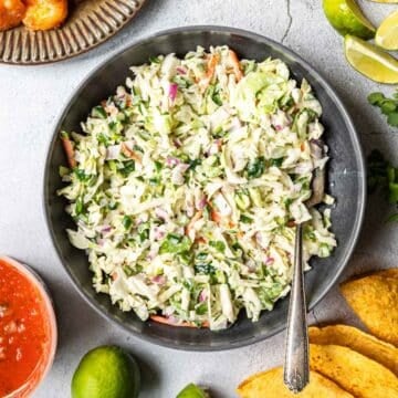 Fish taco slaw in a bowl next to other taco ingredients around it.