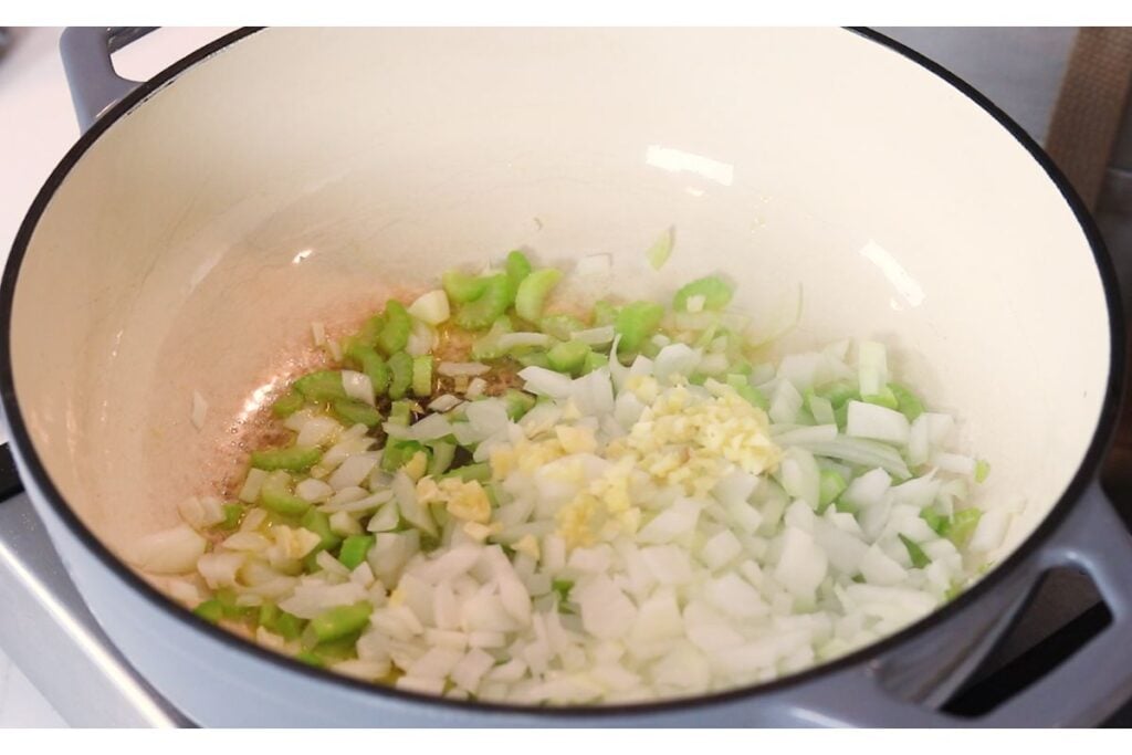 Diced onions and sliced celery sauteeing in a Dutch oven.