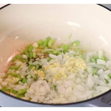 Diced onions and sliced celery sauteeing in a Dutch oven.