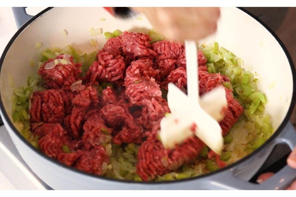 Meat masher chopping up ground hamburger over the softened veggies.