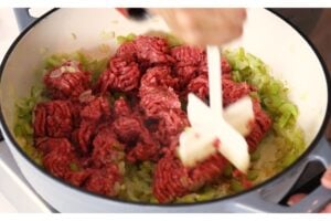 Meat masher chopping up ground hamburger over the softened veggies.
