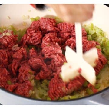 Meat masher chopping up ground hamburger over the softened veggies.