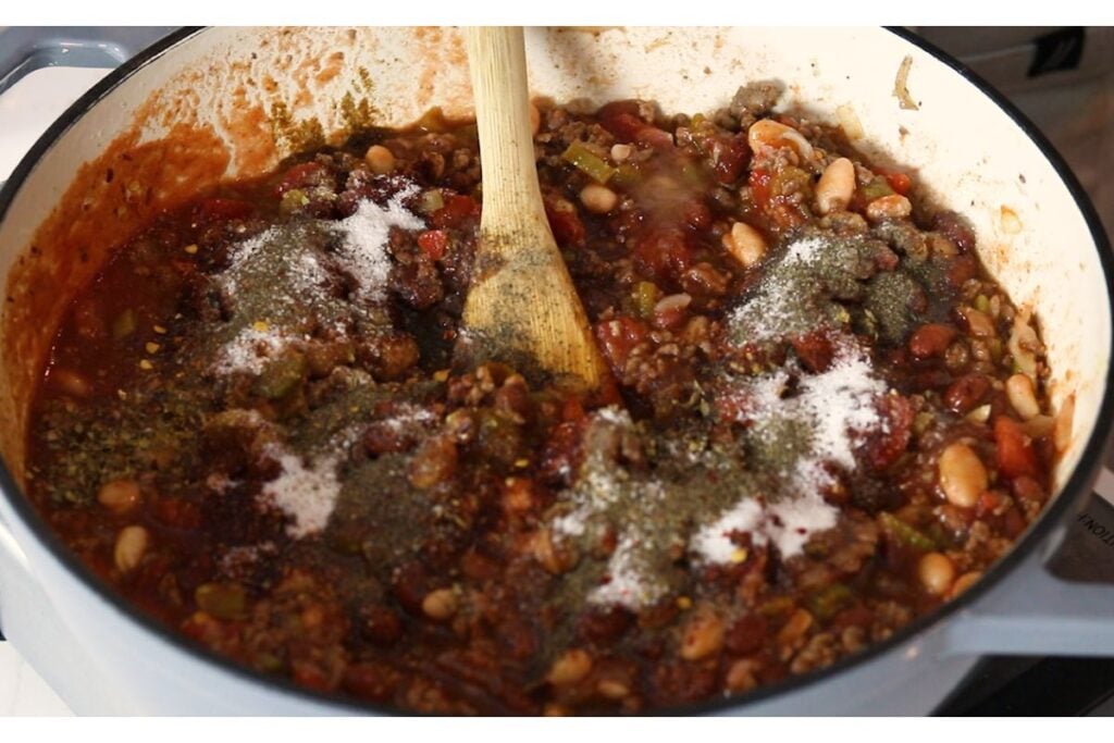 Wooden spoon stirring all the seasonings into the chili mixture.