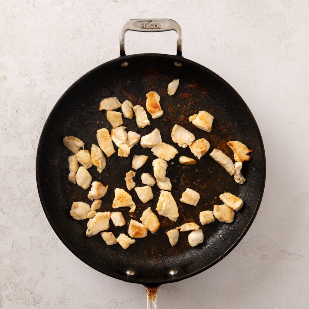 Chicken breast chunks sauteing in a frying pan.