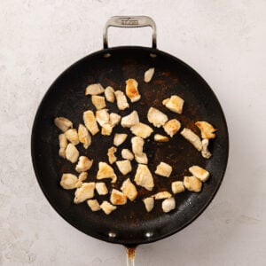 Chicken breast chunks sauteing in a frying pan.