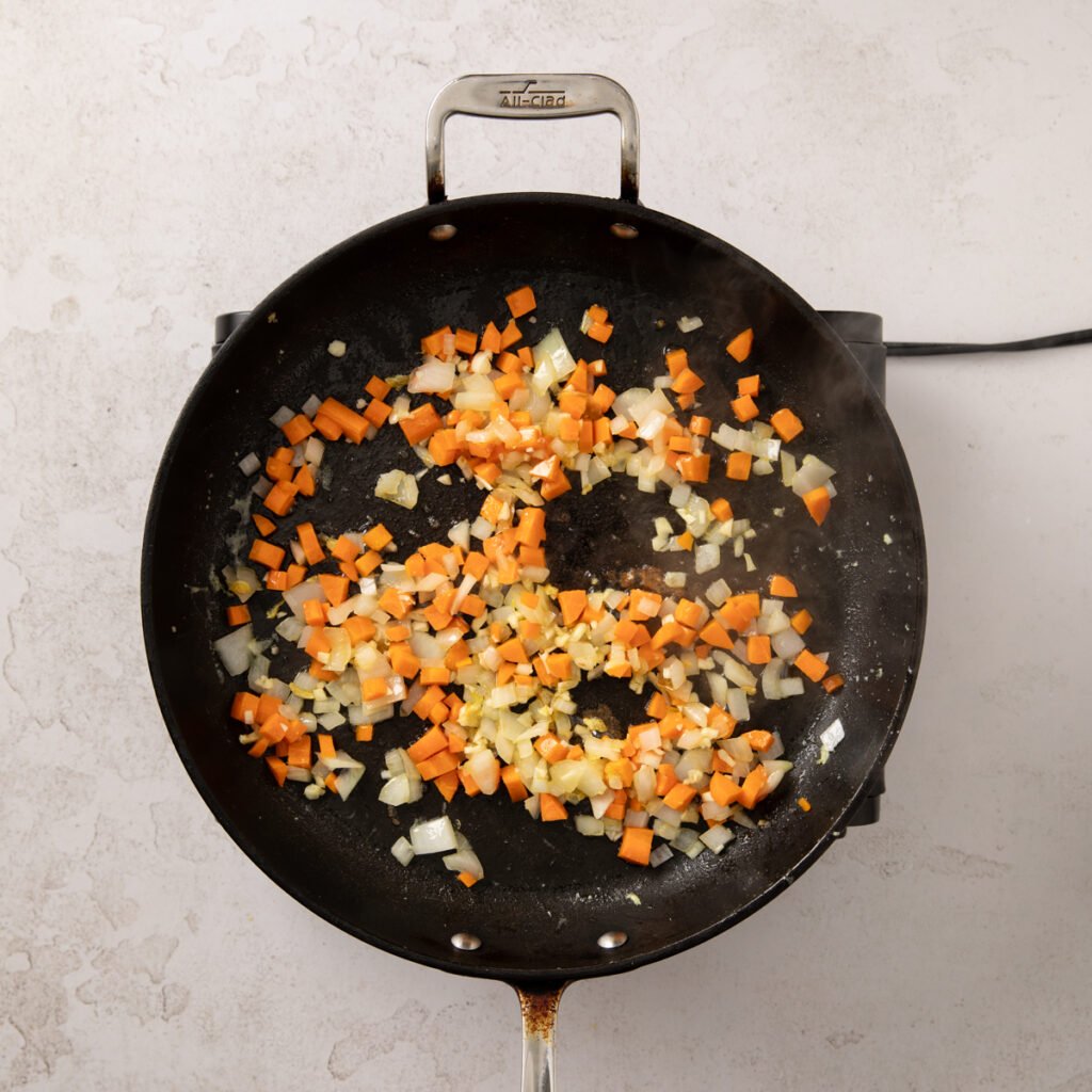 Chopped onions and diced carrots sauteing in a frying pan.