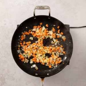 Chopped onions and diced carrots sauteing in a frying pan.