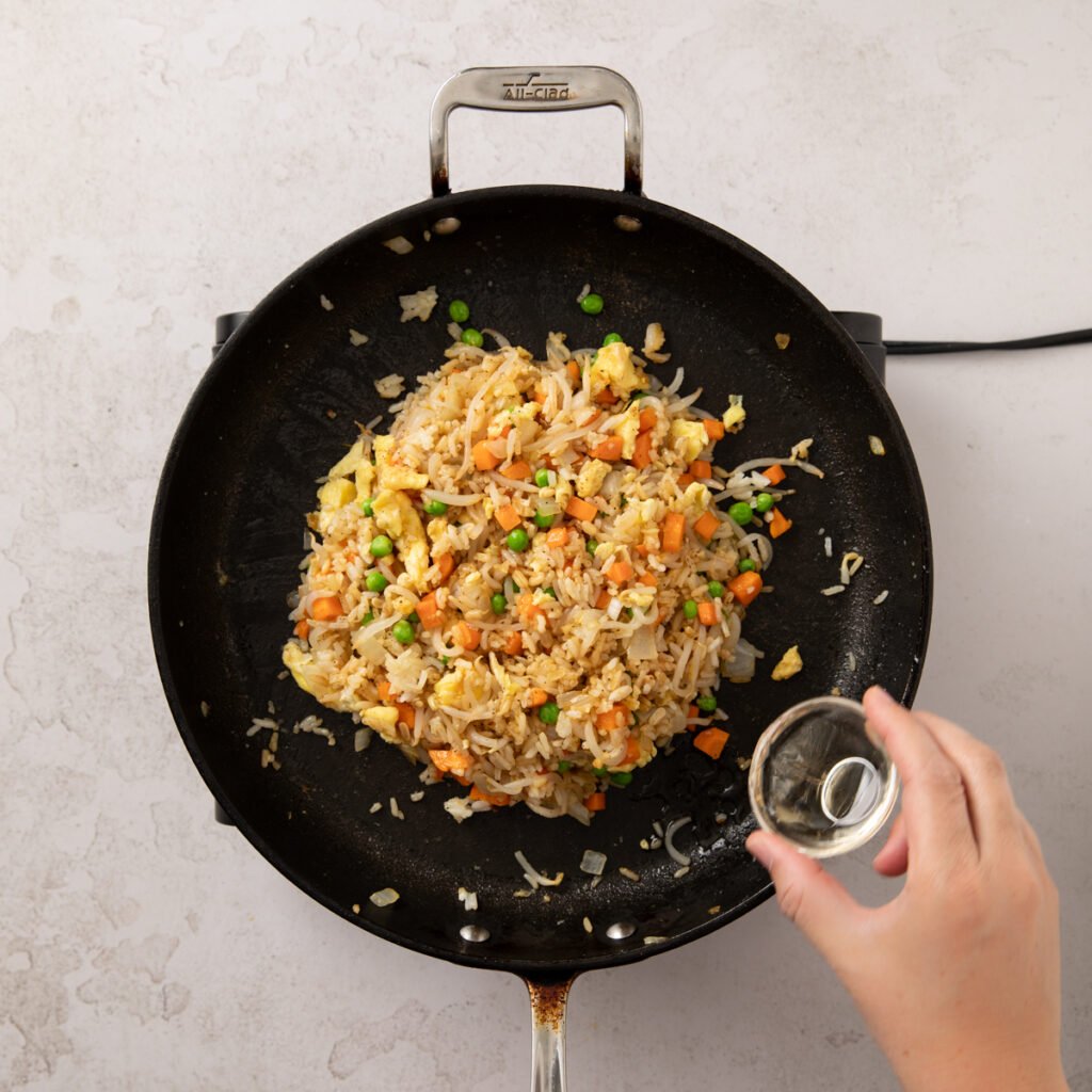 Sauce being added to chicken fried rice in a pan.