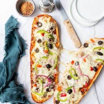Cheesy pull coming between two halved loaves of French bread supreme pizza, ready to serve.
