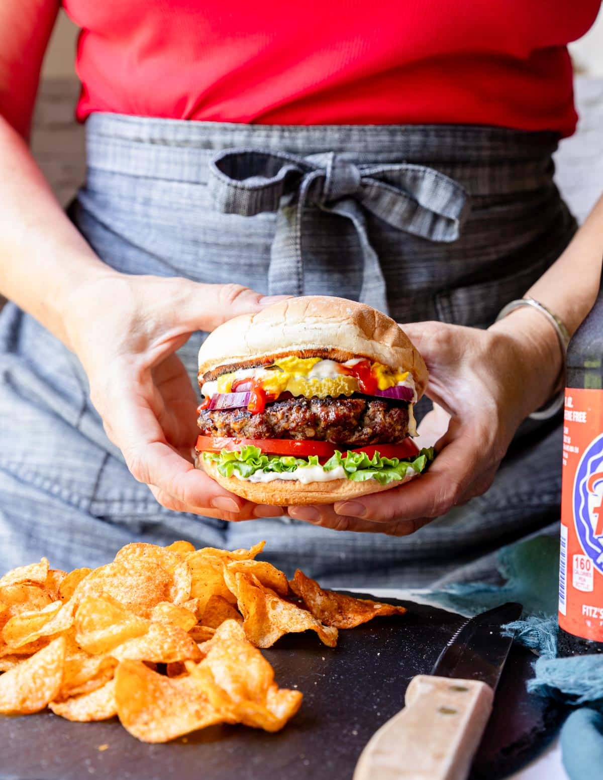 two hands holding a ribeye steak burger on a bun with all the fixings.