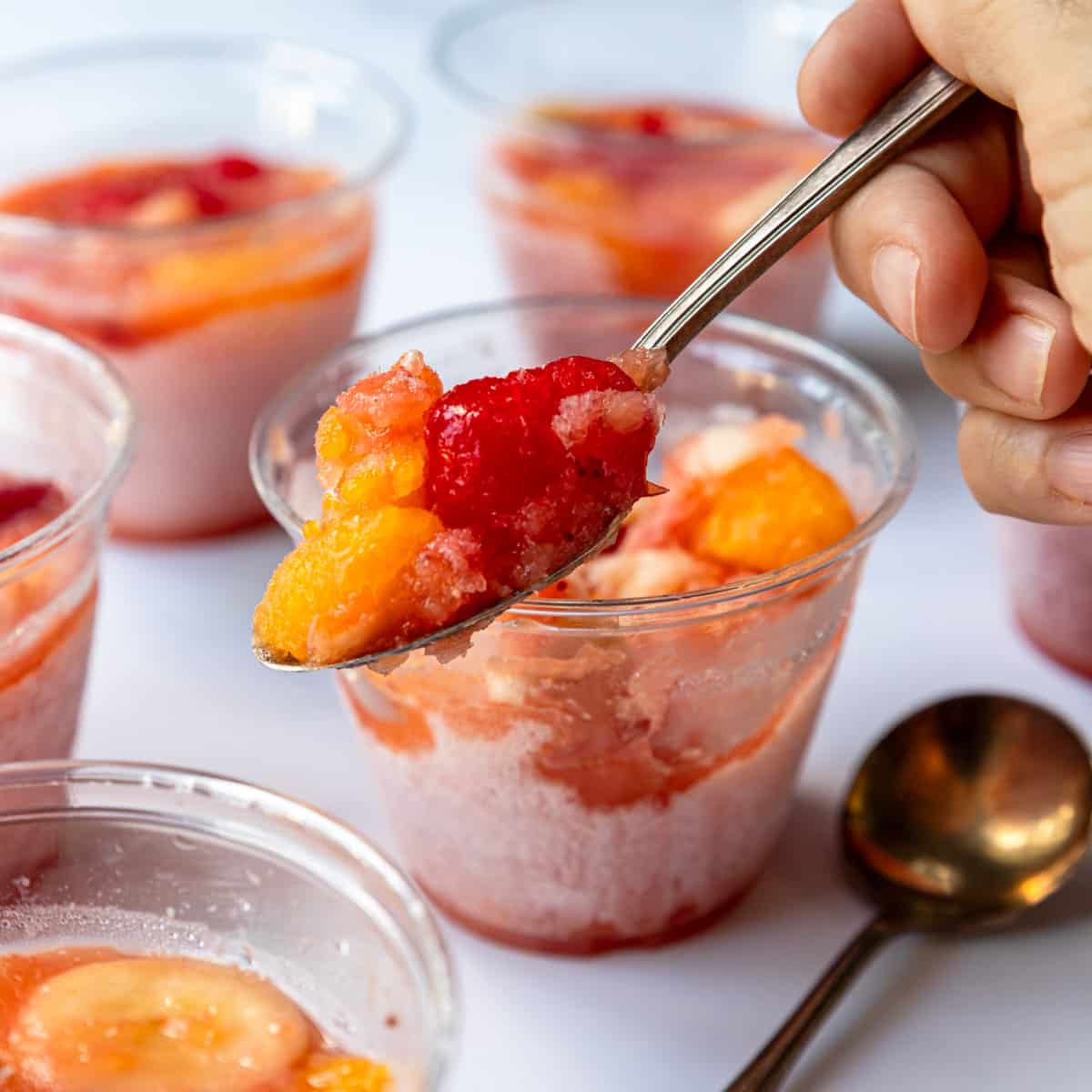 A spoon holding a bite of frozen fruit cup, nice and slushy.