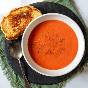 Tomato Gazpacho in a bowl with black pepper sprinkled over top, grilled cheese to the side