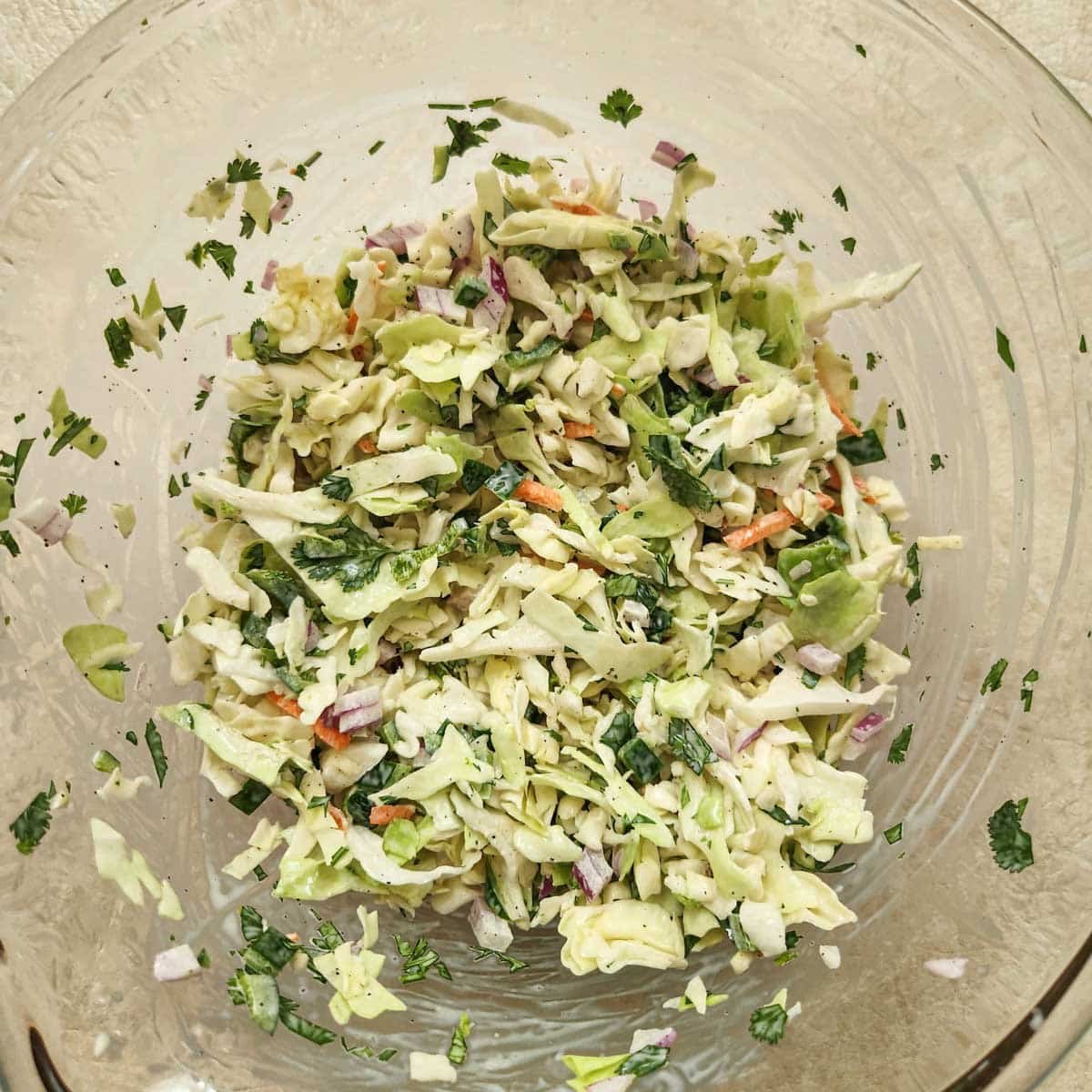 Cabbage mixture combined with the wet ingredients in a glass mixing bowl.
