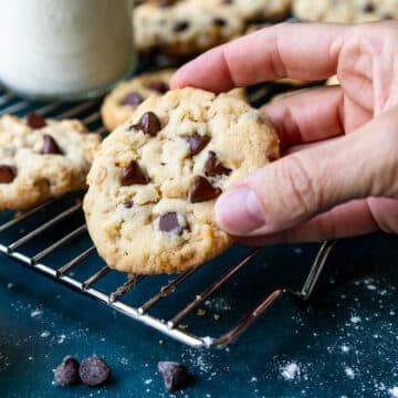 Hand picking up a freshly baked 100 Good cookie from the cooling rack.