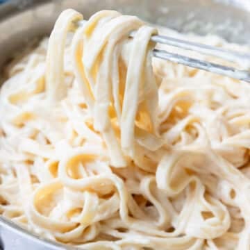 Close up of rich creamy alfredo sauce covering linguine noodles in a saucepan.