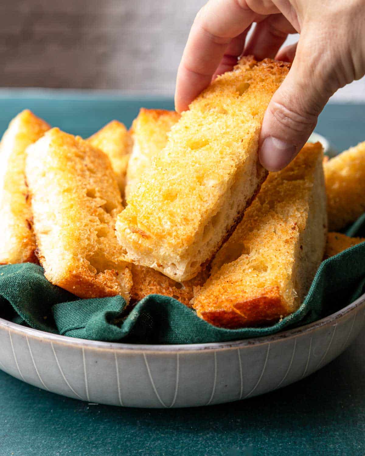 Hand picking up a slice of garlic bread from a basket.