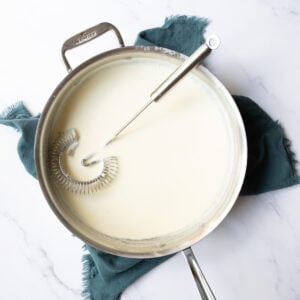 Whisk resting in a pan of thick alfredo sauce for serving with pasta.